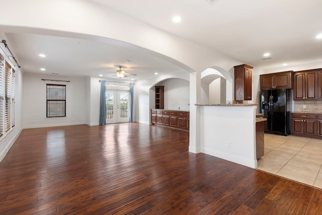 kitchen featuring black fridge with ice dispenser, tasteful backsplash, ceiling fan, light stone countertops, and light hardwood / wood-style floors