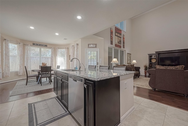 kitchen featuring sink, light tile patterned floors, dishwasher, light stone counters, and an island with sink