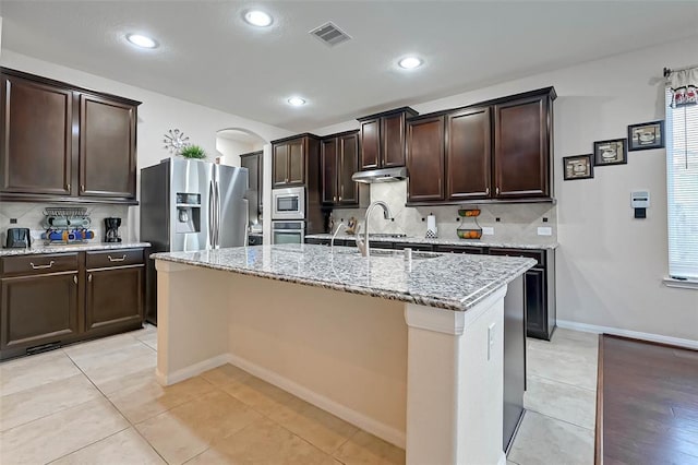 kitchen featuring appliances with stainless steel finishes, tasteful backsplash, an island with sink, sink, and dark brown cabinets