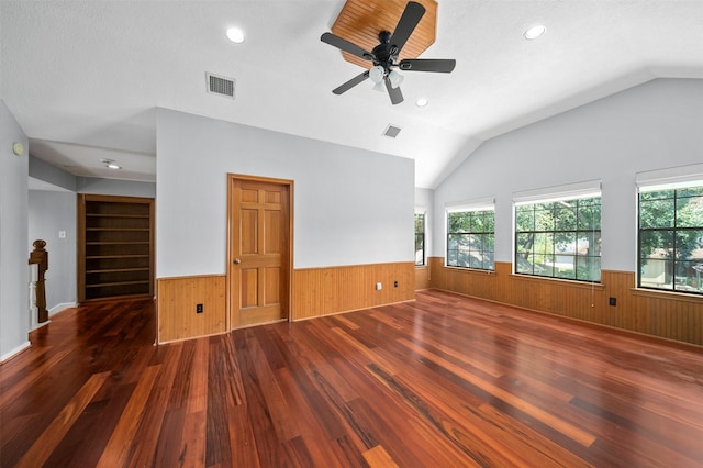 unfurnished living room featuring lofted ceiling, a wealth of natural light, and wooden walls