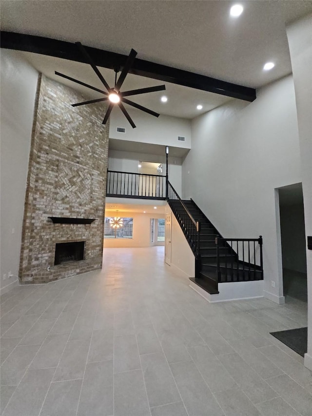 unfurnished living room featuring a brick fireplace, beam ceiling, a textured ceiling, and a towering ceiling