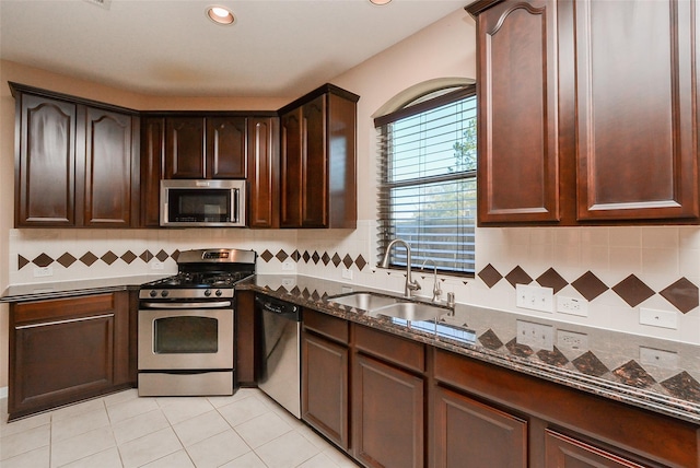 kitchen featuring sink, dark brown cabinets, stainless steel appliances, light tile patterned flooring, and dark stone counters