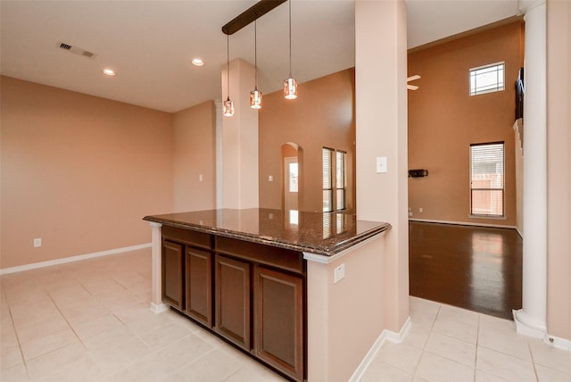 kitchen with light tile patterned floors, dark stone countertops, hanging light fixtures, a towering ceiling, and dark brown cabinets