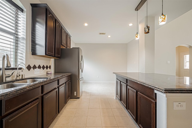 kitchen with arched walkways, decorative light fixtures, tasteful backsplash, a sink, and dark brown cabinetry