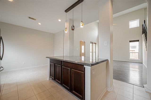 kitchen with arched walkways, light tile patterned flooring, stone countertops, dark brown cabinetry, and decorative light fixtures