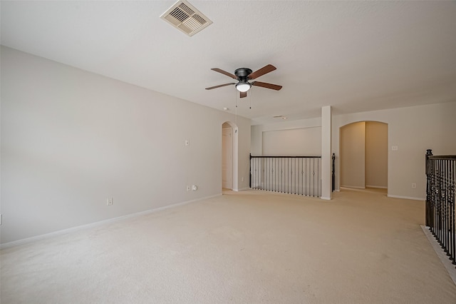 empty room with arched walkways, ceiling fan, light carpet, visible vents, and baseboards