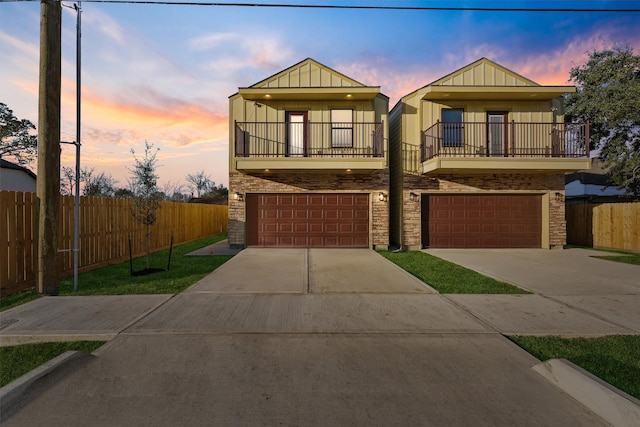 view of front of home with an attached garage, board and batten siding, fence, a balcony, and driveway