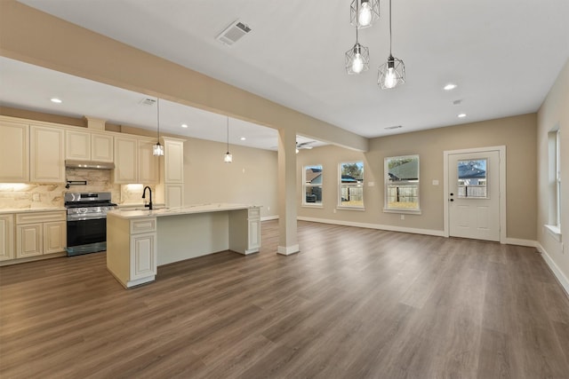 kitchen featuring stainless steel range oven, tasteful backsplash, light stone counters, decorative light fixtures, and dark hardwood / wood-style flooring