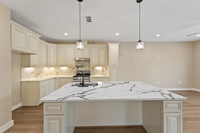 kitchen with decorative light fixtures, light stone countertops, a center island with sink, and stainless steel gas range oven