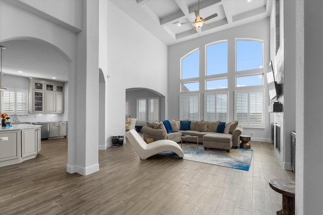 living room featuring ceiling fan, beam ceiling, a towering ceiling, coffered ceiling, and light wood-type flooring