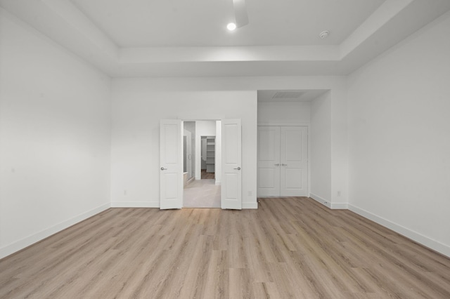 unfurnished bedroom featuring ceiling fan, a raised ceiling, light hardwood / wood-style floors, and a closet