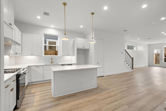 kitchen with sink, stainless steel gas range oven, decorative light fixtures, a center island, and white cabinets