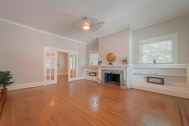 unfurnished living room featuring french doors, ornamental molding, hardwood / wood-style flooring, ceiling fan, and a fireplace