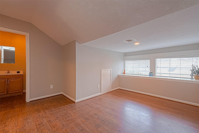 unfurnished room with sink, hardwood / wood-style flooring, vaulted ceiling, and a textured ceiling