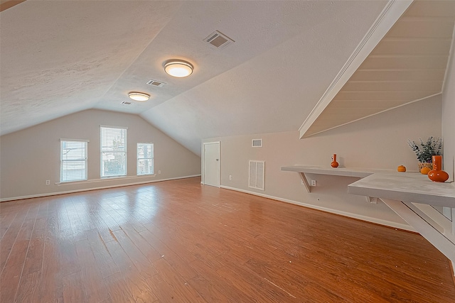 bonus room with hardwood / wood-style flooring, vaulted ceiling, and a textured ceiling