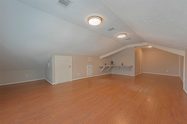 additional living space featuring hardwood / wood-style flooring, vaulted ceiling, and a textured ceiling