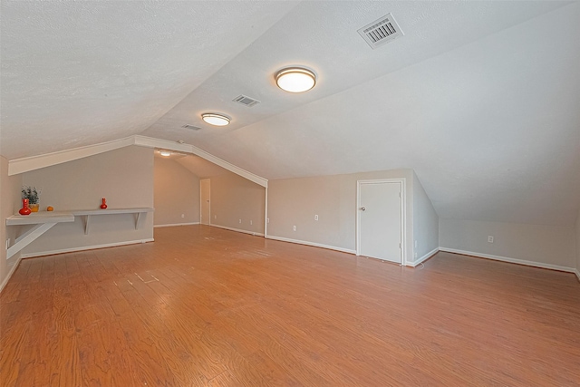 bonus room with vaulted ceiling, light hardwood / wood-style floors, and a textured ceiling