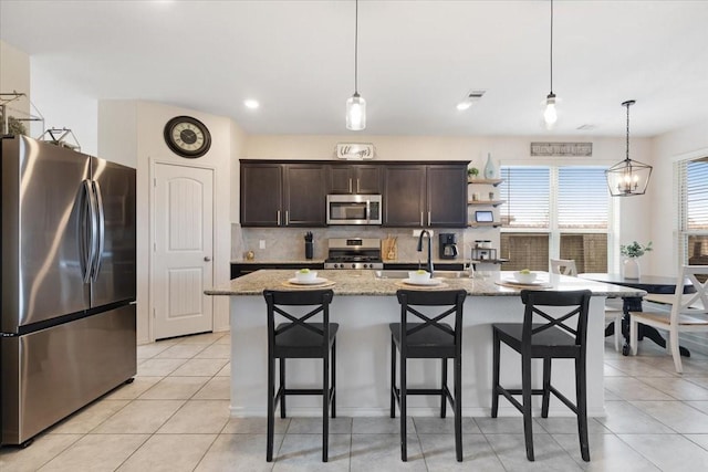 kitchen with pendant lighting, an island with sink, sink, light stone counters, and stainless steel appliances