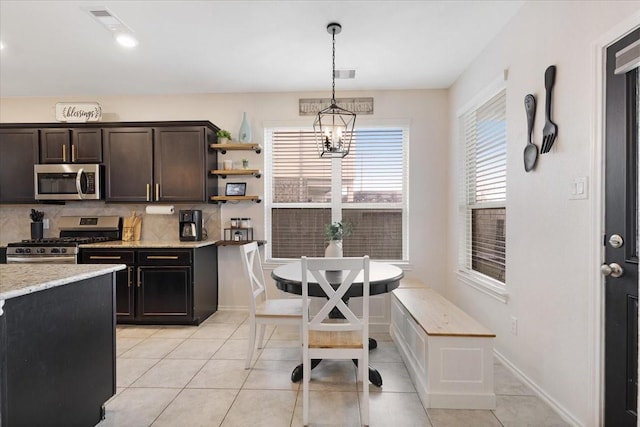 kitchen featuring light tile patterned floors, appliances with stainless steel finishes, backsplash, dark brown cabinetry, and decorative light fixtures