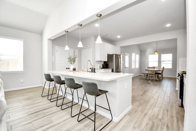 kitchen featuring appliances with stainless steel finishes, decorative light fixtures, lofted ceiling, white cabinets, and a kitchen bar