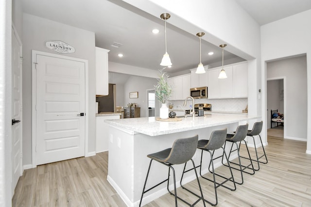 kitchen with white cabinetry, light stone counters, decorative light fixtures, light hardwood / wood-style flooring, and backsplash