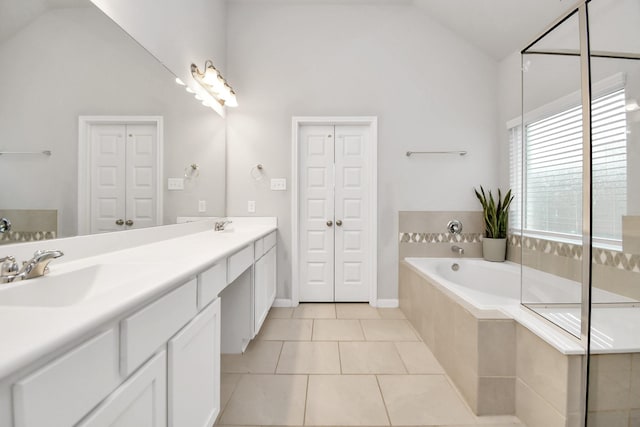 bathroom featuring tile patterned flooring, vanity, lofted ceiling, and tiled bath