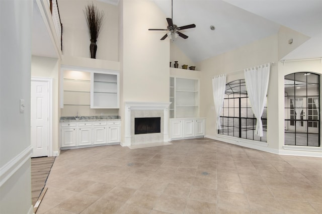 unfurnished living room with built in shelves, sink, high vaulted ceiling, ceiling fan, and a high end fireplace