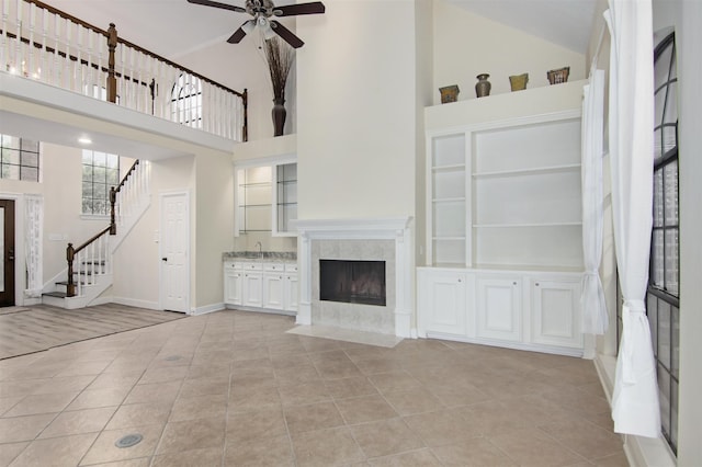 unfurnished living room with ceiling fan, a towering ceiling, a fireplace, and light tile patterned flooring