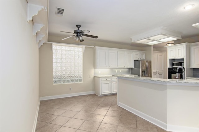 kitchen with white cabinetry, stainless steel fridge, decorative backsplash, light tile patterned floors, and light stone counters