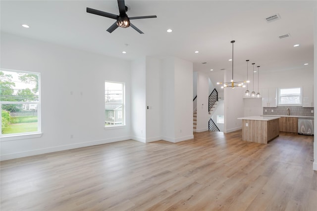 unfurnished living room with ceiling fan with notable chandelier, a wealth of natural light, and light wood-type flooring