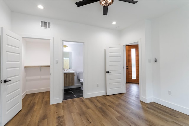 unfurnished bedroom with ensuite bathroom, a walk in closet, wood-type flooring, a closet, and ceiling fan