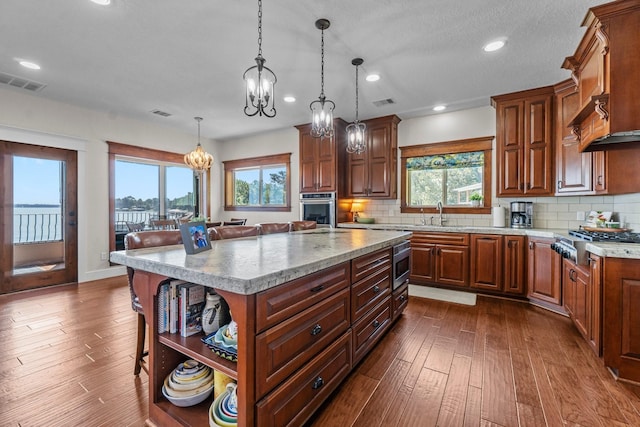 kitchen with appliances with stainless steel finishes, dark hardwood / wood-style floors, a kitchen island, pendant lighting, and backsplash