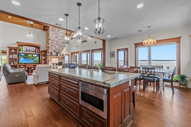 kitchen with a center island, stainless steel microwave, a kitchen breakfast bar, a fireplace, and light stone countertops