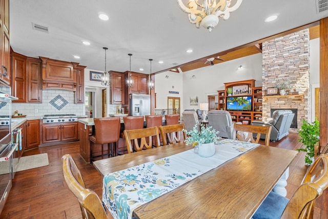 dining space with a stone fireplace, dark wood-type flooring, and a notable chandelier