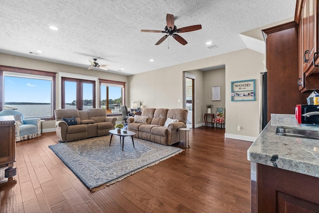 living room featuring sink, ceiling fan, a water view, a textured ceiling, and dark hardwood / wood-style flooring