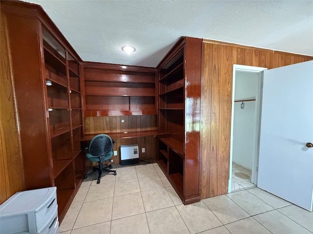 office space with built in desk, wooden walls, a textured ceiling, and light tile patterned flooring