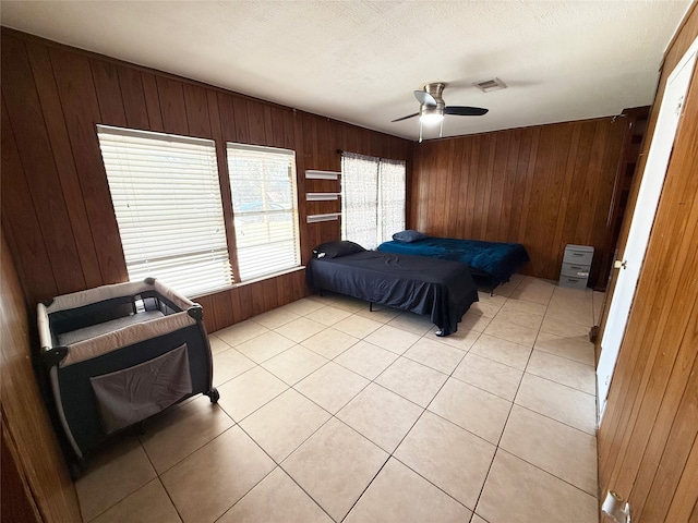 bedroom featuring ceiling fan, light tile patterned floors, a textured ceiling, and wood walls