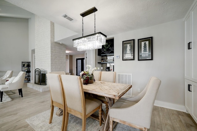 dining room with a fireplace, a chandelier, light hardwood / wood-style flooring, and a textured ceiling