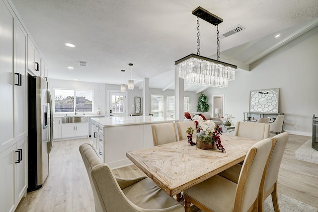 dining room featuring lofted ceiling, a textured ceiling, a chandelier, and light wood-type flooring