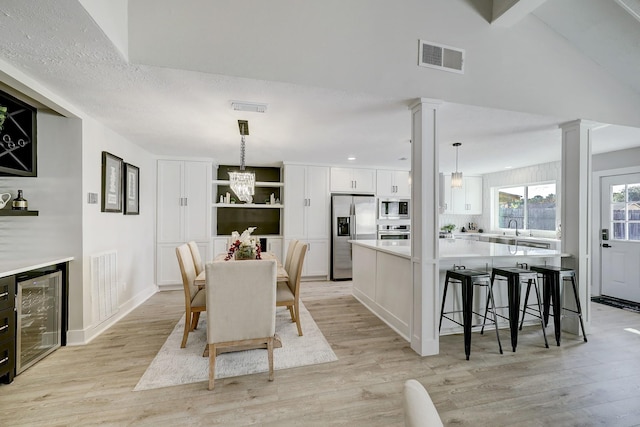 dining area featuring light hardwood / wood-style floors, sink, decorative columns, and beverage cooler