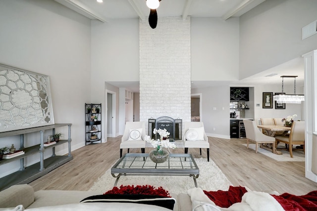 living room featuring a brick fireplace, light hardwood / wood-style floors, beamed ceiling, and a high ceiling