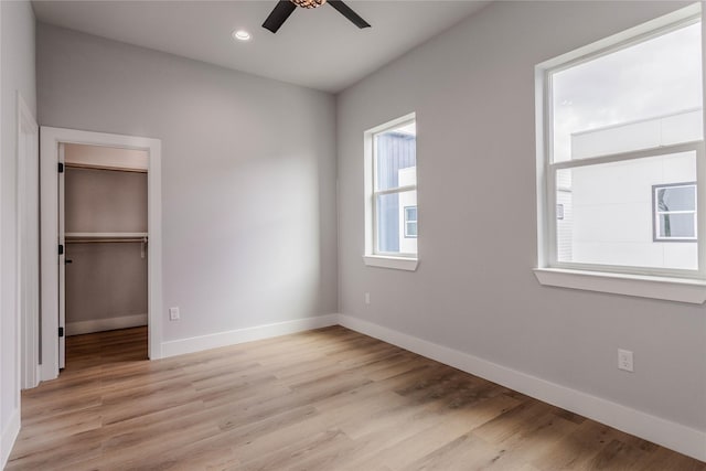 unfurnished bedroom featuring ceiling fan, a spacious closet, light hardwood / wood-style floors, and a closet