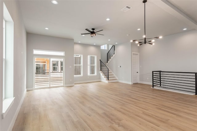 unfurnished living room featuring plenty of natural light, ceiling fan with notable chandelier, and light hardwood / wood-style floors