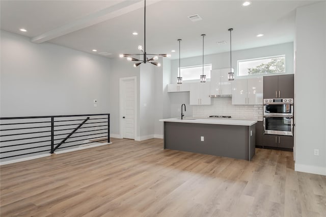 kitchen with sink, a kitchen island with sink, hanging light fixtures, light hardwood / wood-style floors, and white cabinets