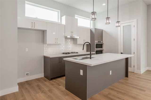 kitchen with sink, white cabinetry, tasteful backsplash, an island with sink, and decorative light fixtures