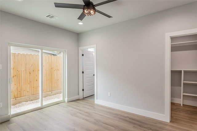 unfurnished bedroom with access to exterior, a walk in closet, light hardwood / wood-style floors, and ceiling fan