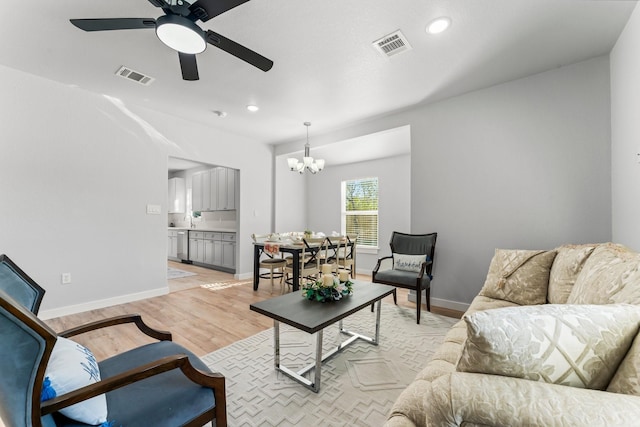 living room with ceiling fan with notable chandelier and light wood-type flooring