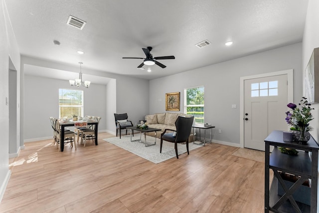 living room featuring ceiling fan with notable chandelier, a textured ceiling, and light wood-type flooring