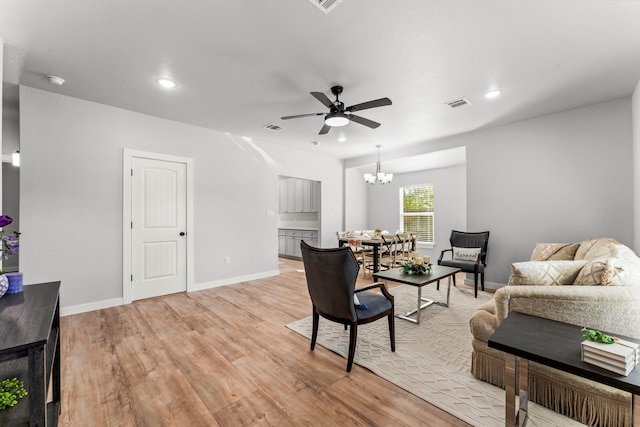 living room with ceiling fan with notable chandelier and light hardwood / wood-style flooring