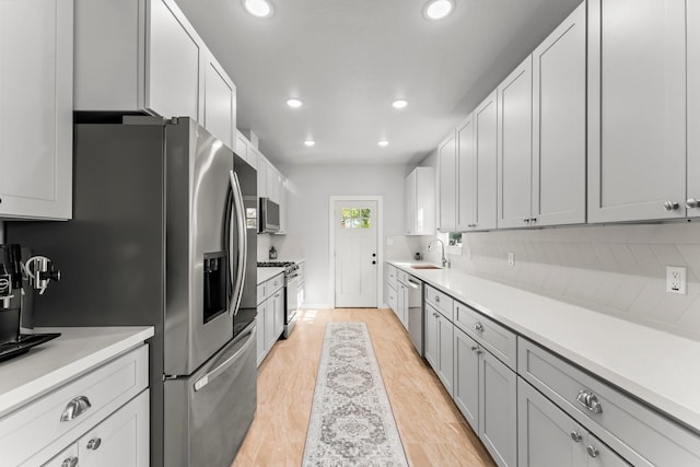 kitchen with sink, white cabinets, decorative backsplash, stainless steel appliances, and light hardwood / wood-style flooring